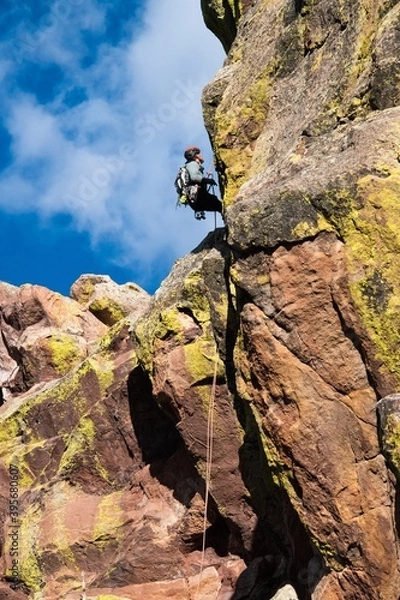 Fototapeta Climber repelling down from a tall multicolored rock face in Boulder Colorado. The climber is using climbing equipment to descend from one of the Flatirons