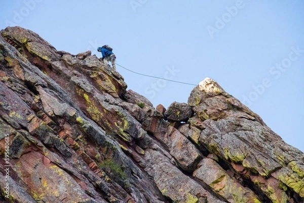 Fototapeta Person climbing up a tall multicolored rock face in Boulder Colorado. The climber is using climbing equipment to ascend one of the Flatirons
