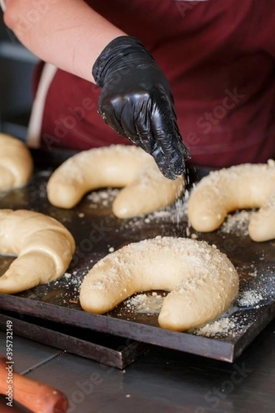Fototapeta a woman's gloved hand sprinkles bagels in a bakery