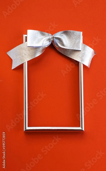 Obraz Bright holiday background. An empty silver frame and a bow on a red background. Concept greetings for Christmas, thanksgiving, New year, mother's Day, birthday, Valentine's Day