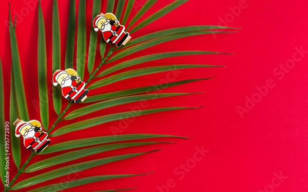 Obraz New year's holiday background. Palm branch with wooden figures of Santa Claus on a red background. The view from the top. Greeting card for Christmas.