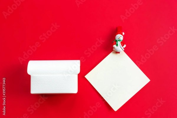 Obraz An empty gift box and a white sheet of paper with a snowman figure on a red background. Concept greetings for Christmas, New year. Flat lay, copy space, horizontal cropping