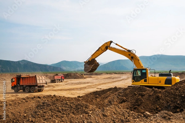 Fototapeta  Earthworks on a summer day in a mountainous area. Excavators load soil into the tipper body