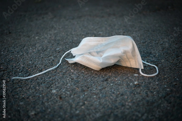 Fototapeta Crumpled used disposable protective medical mask on the asphalt. Black and white photo with vignetting.
