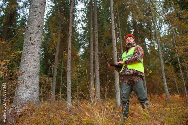 Fototapeta A forest engineer in a helmet and a vest works in the forest with a computer. The concept of computerized forest inventory.