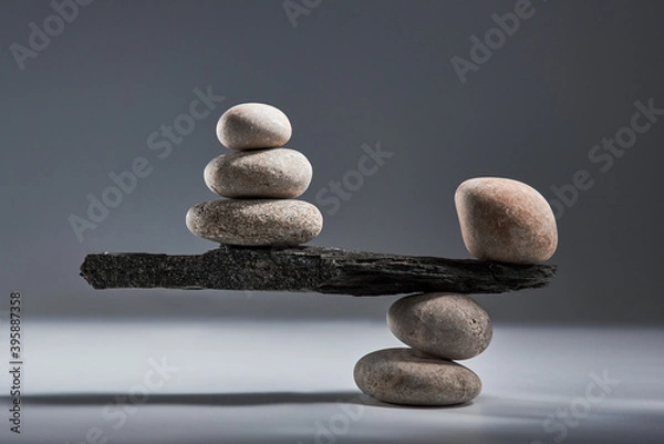 Fototapeta Balancing pyramid of sea pebbles on a gray background, the concept of harmony and balance, heavy and light. Stones in the form of scales with balancing stones.