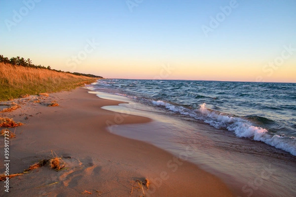 Obraz Golden sunset on a wide sandy beach along the coast of Lake Michigan as waves crash onto the shore.