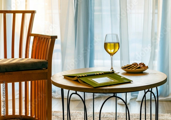 Obraz Still life with white wine and a book on a coffee table against the background of a window