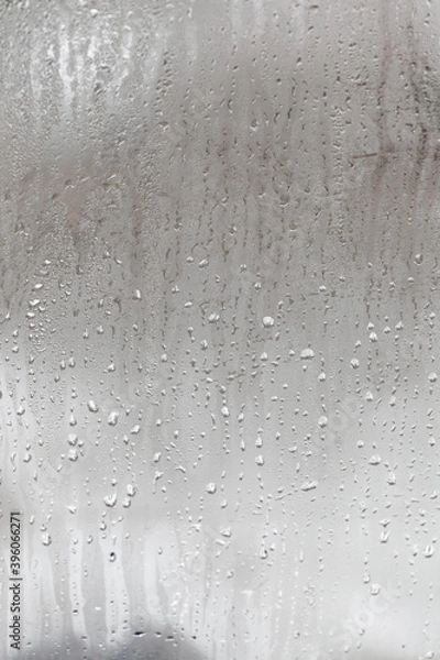 Obraz Natural drops of water flow down the glass, high humidity in the room, condensation on the glass window. Neutral colors. Vertical photo orientation