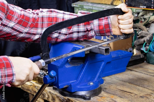 Obraz A worker is cutting by hacksaws metal profile. A handyman with hacksaws for metal. A locksmith vise