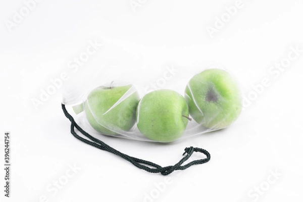 Fototapeta Three fresh sour healthy green apples on a white background are in an eco-friendly reusable bag-grid from the supermarket