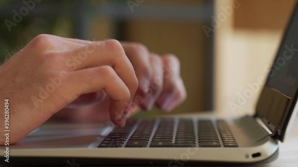 Fototapeta Close up shot of male hands typing on laptop while sitting at office desk indoors. Man fingers tapping and texting on computer keyboard while working in cabinet. 