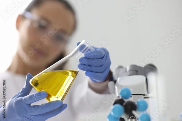 Fototapeta Researcher holds flask with yellow liquid. Research of properties of oil and oil products concept