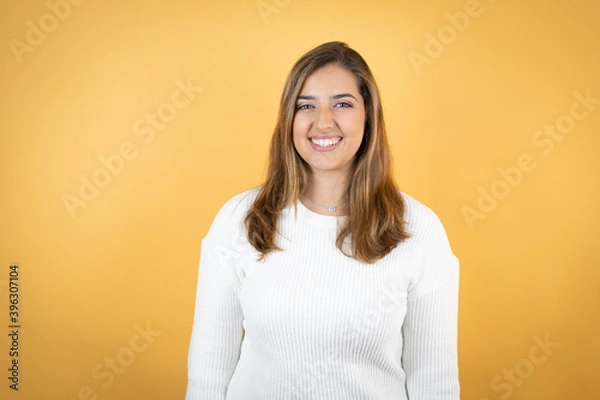 Fototapeta Young caucasian woman over isolated yellow background with a happy face standing and smiling with a confident smile showing teeth