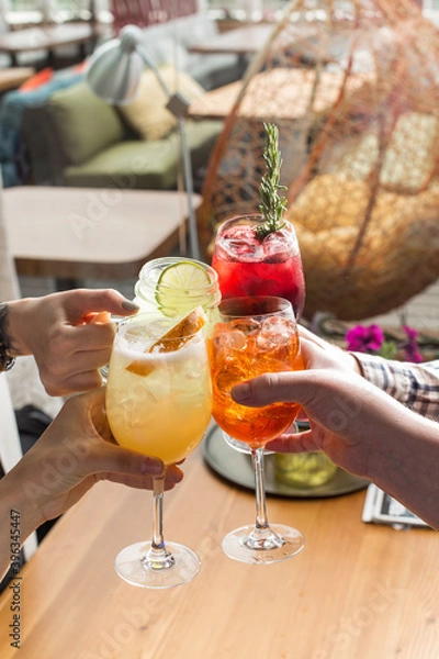 Obraz Friends toasting saying cheers hands holding summer cold cocktail drinks on cafe background