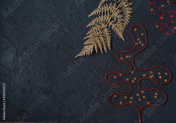 Fototapeta Golden artificial branch, red ornaments in the form of a Christmas tree and gold stars on a black background.