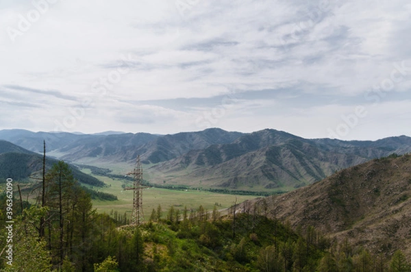 Obraz Photo of a Mountain summer Landscape. Travel location of popular tourist attraction. View of beautiful nature. Grassy field, hills, power lines on cloudy sky background.