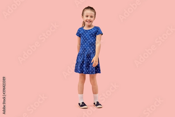Fototapeta Little brunette girl dancing in a blue dress with a little star print in sneakers. Pink isolated background.