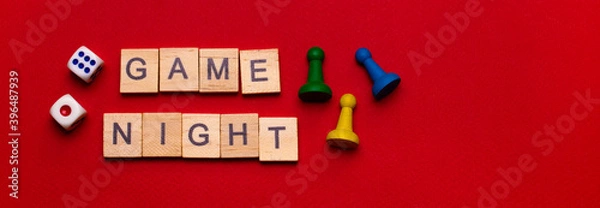Fototapeta Wooden block lettering "Game night" on a red texture background surrounded by yellow and green game chips and game cube: Board game banner