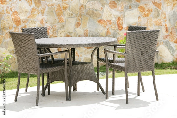 Obraz Table and chairs in a tropical garden with a stone wall texture