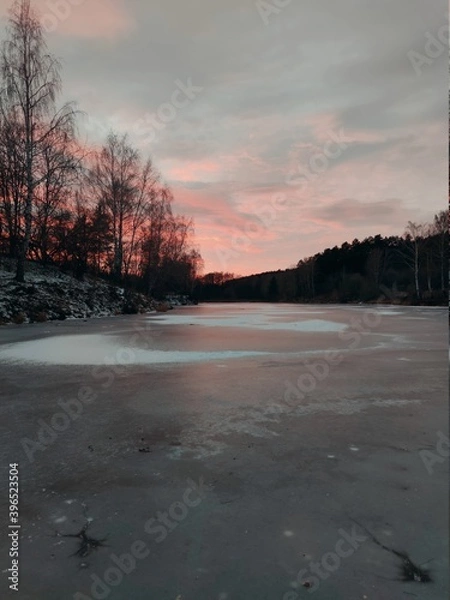 Fototapeta frozen surface of the lake against the background of sunset in a beautiful evening landscape