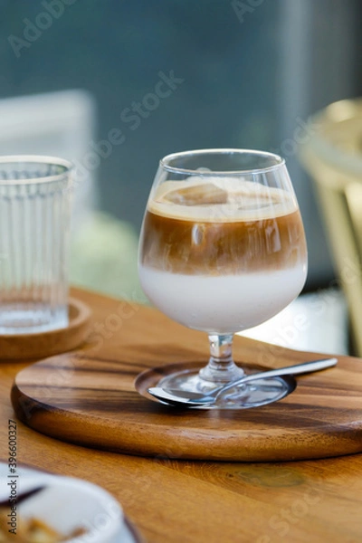 Fototapeta selective focus, wine glass of iced coffee two layers fresh milk and espresso short on wooden table at cafe. Refreshing summer drink concept