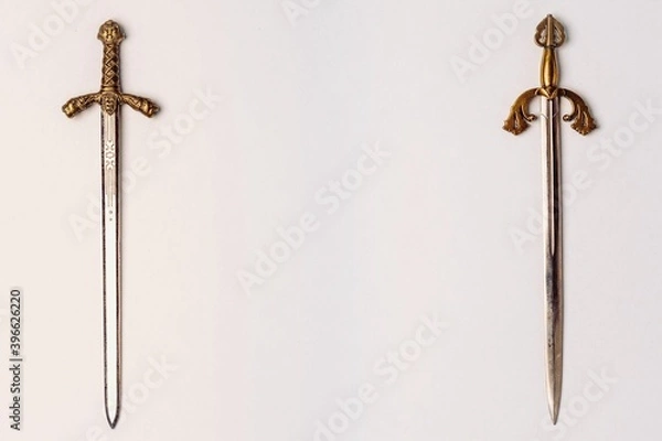 Fototapeta Two ancient knightly swords with golden hilts with engraving isolated on a white background. Horizontal position, copy space