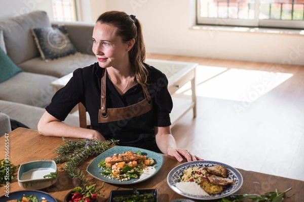 Fototapeta Young attractive swedish food blogger posing in front of a table full of food dishes. Young girl sitting in front of a wooden table eating vegetarian food and healthy dishes. Vegetarian lifestyle