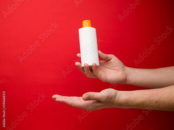 Fototapeta Hand holding white shampoo bottle isolated on red background.