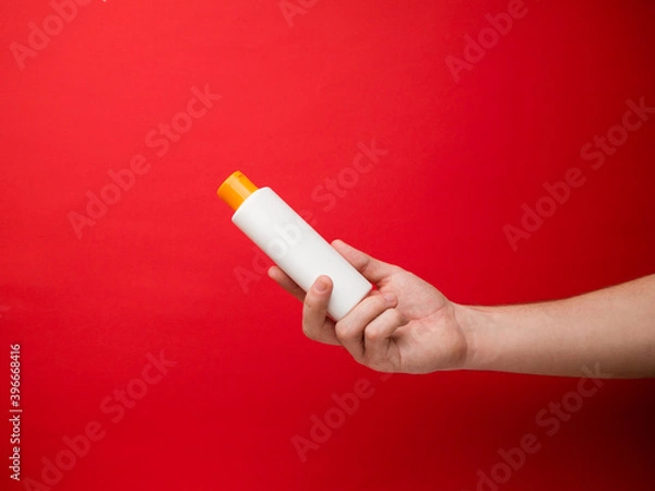 Obraz Hand holding white shampoo bottle isolated on red background.