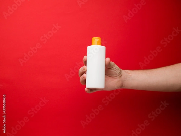 Obraz Hand holding white shampoo bottle isolated on red background.