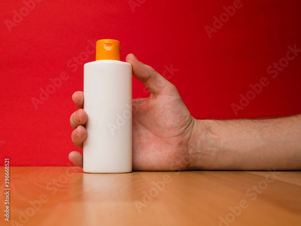 Obraz Hand holding white shampoo bottle isolated on red background.