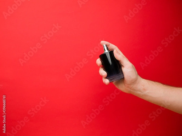 Fototapeta Hand of European men holding perfume. Isolated on red background. Studio portrait.