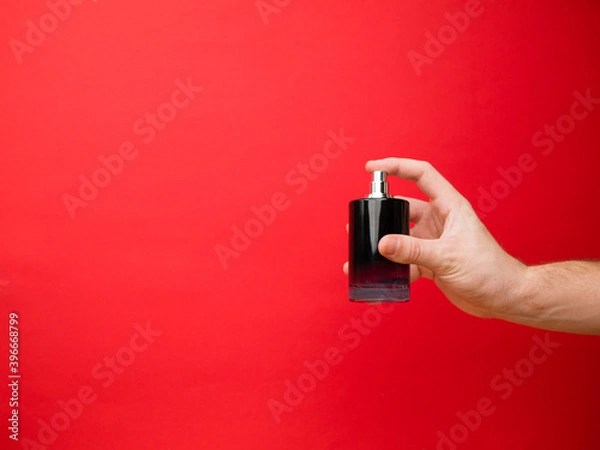 Fototapeta Hand of European men holding perfume. Isolated on red background. Studio portrait.
