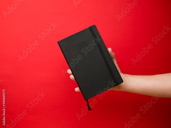 Obraz Hand of European men holding black note. Isolated on red background. Studio portrait.