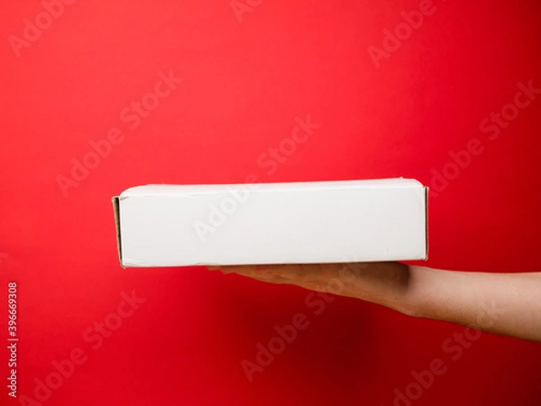 Fototapeta White box on male hand. Food shipping. Fast delivery service. Mockup style and copy space. Cardboard concept. Isolated on red.