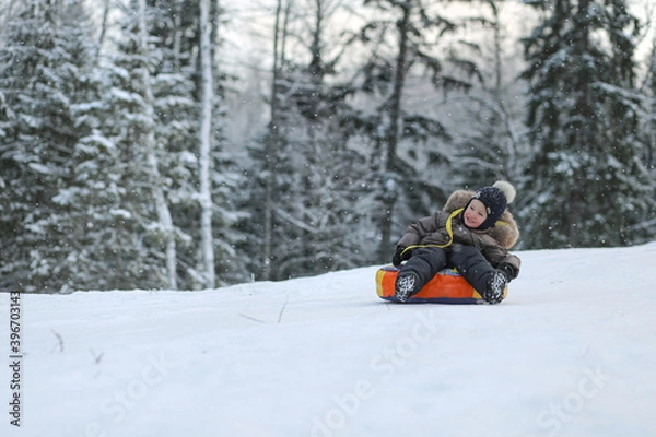 Fototapeta A child riding a tubing from a snow slide in a winter forest. Image with selective focus.