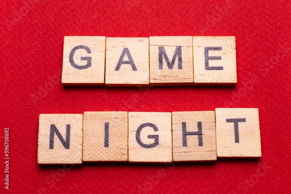 Fototapeta Wooden block lettering "Game night" on a red texture background: Board game background with space for text, minimalism