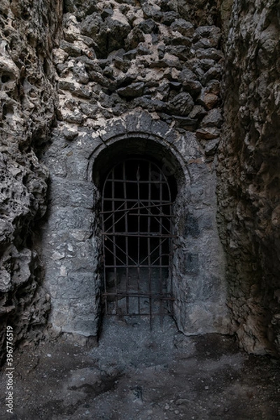 Obraz The entrance to a dark dungeon in the mountain, closed by a rusty metal grating