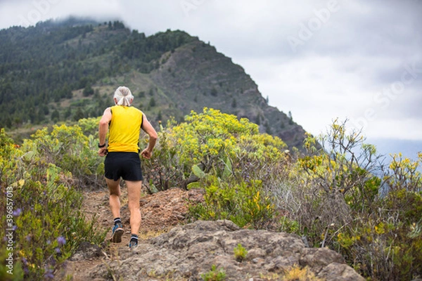 Obraz Old man in yellow t-shirt running on the trail to the mountains of canary island la palma