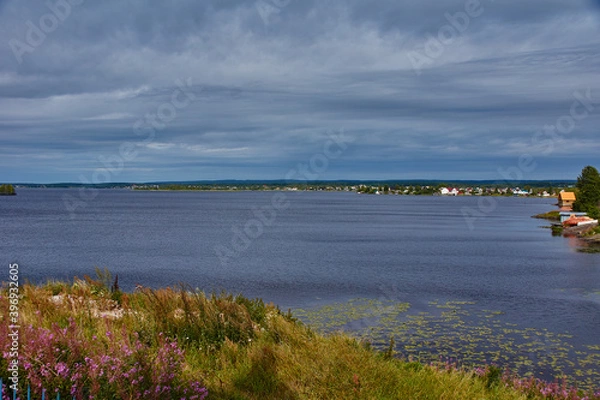 Obraz View of the lake surface.The wide surface of the lake is covered with small ripples. The opposite bank is overgrown with coniferous trees. Individual clouds are visible in the sunny sky. Russia