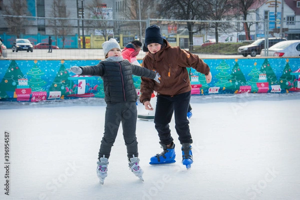 Fototapeta On a frosty winter day, brother and sister go ice skating on the ice rink.