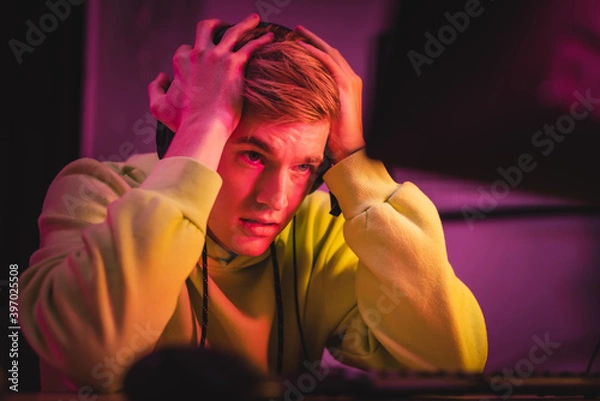 Fototapeta Tensed gamer looking at computer monitor on blurred foreground