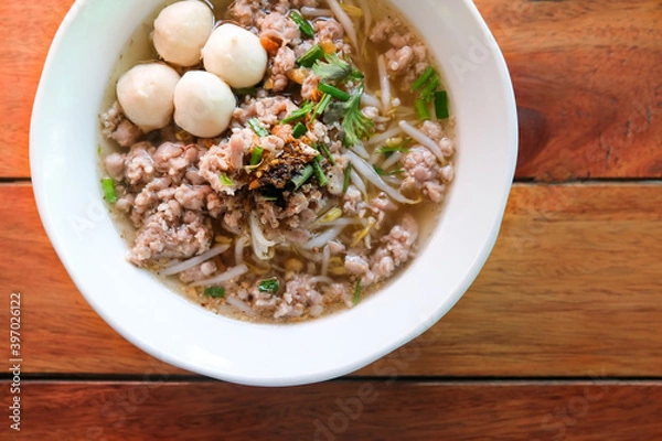 Fototapeta Top view of pork noodles clear soup with minced pork, pork balls and sprouts on the wooden table.