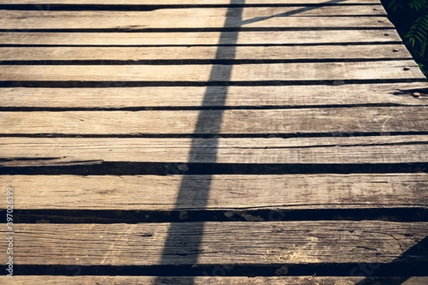Fototapeta Texture of rustic wooden planks bridge against long shadow lines of fence.