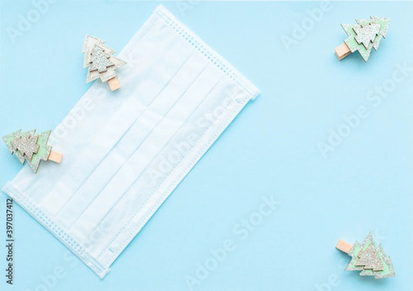 Obraz medical protective face mask and figures of Christmas trees and snowflakes wooden on a blue background. Decor Christmas and New Year 2021. Holidays self-isolation and coronavirus pandemic concept