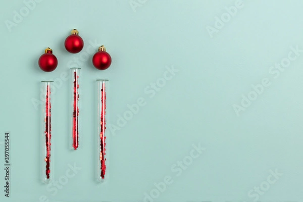 Fototapeta Medical test tubes with red sparkles inside lie next to Christmas balls on a mint green background. Festive flat lay with copy space.
