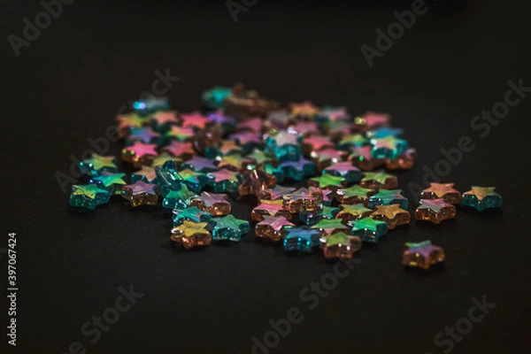 Fototapeta Star-shaped multicolored beads are scattered on a black background. Needlework materials close-up.