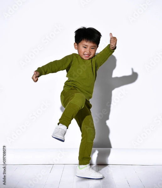 Obraz Fashion portrait of cute little kid boy in stylish green tracksuit dancing break against white studio wall. The concept of sports and healthy activities for the modern child.