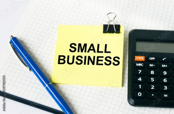 Fototapeta Calculator with a blue pen and a yellow sticker with text Small Business lie down on notepad